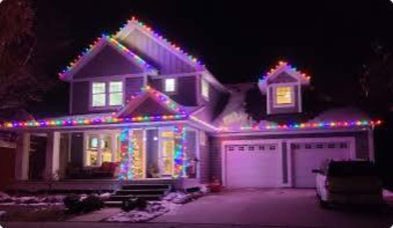 A two-story home outlined with multicolor Christmas lights at night.